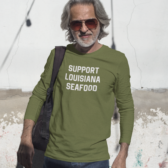 Man wearing a green shirt with 'Support Louisiana Seafood' text, standing near water.